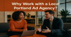 Two professionals sit on a couch in a Portland, Oregon office, engaged in conversation with a laptop in front of them. Text above reads, "Why Work with Local Ad Agencies in 2025?.